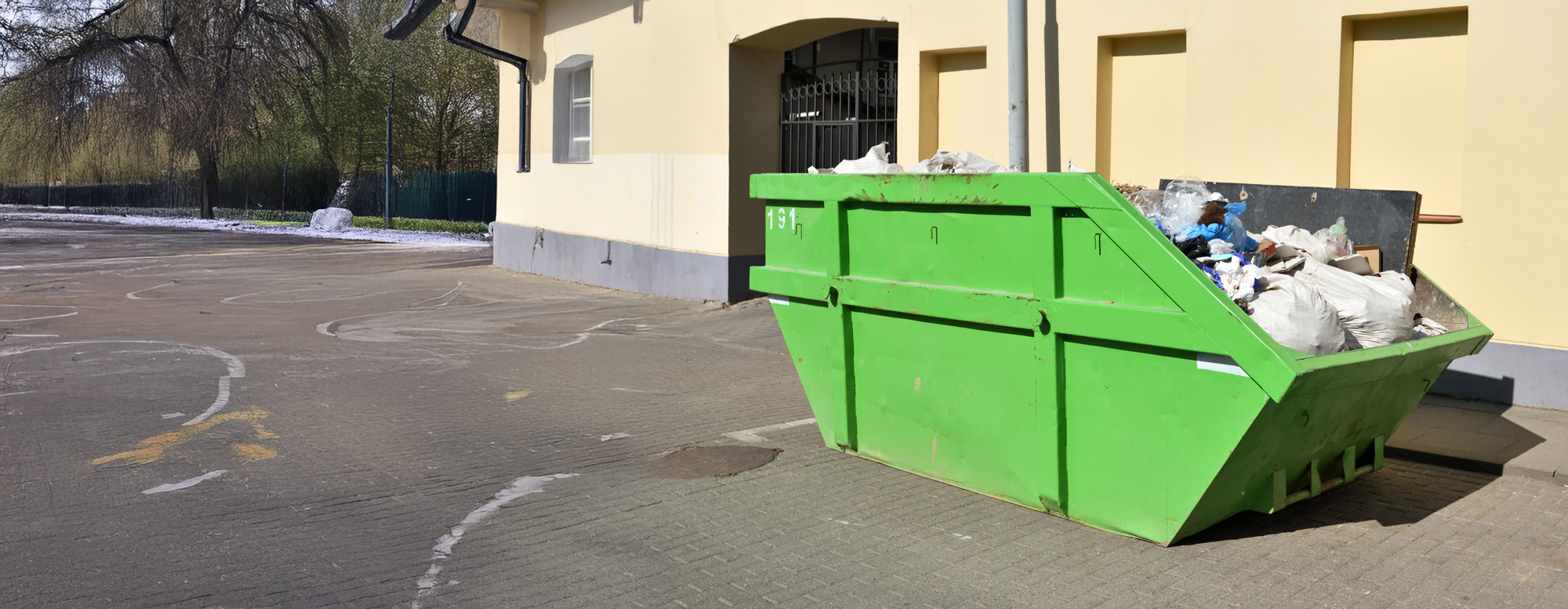 entsorgung-unrat Grüner Container vor einem Gebäude.